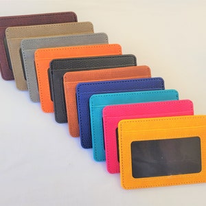 May include: Ten leather card holders in various colors, including brown, beige, gray, orange, black, blue, turquoise, pink, and yellow. Each holder has a clear window for displaying identification.