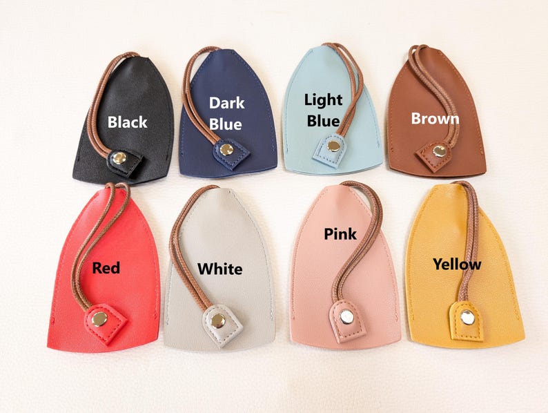 May include: Eight leather keychains in different colors, including black, dark blue, light blue, brown, red, white, pink, and yellow. Each keychain has a loop for attaching keys and a small metal tag with the color name printed on it.