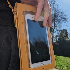 May include: A mustard yellow crossbody phone case with a clear plastic window to display a smartphone. The case has a gold chain strap.