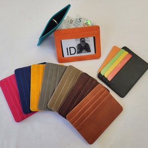 May include: Assortment of leather card holders in various colors, including orange, brown, gray, blue, and pink. Some card holders have a clear window for an ID card.  The text "ID" is visible on one of the card holders.