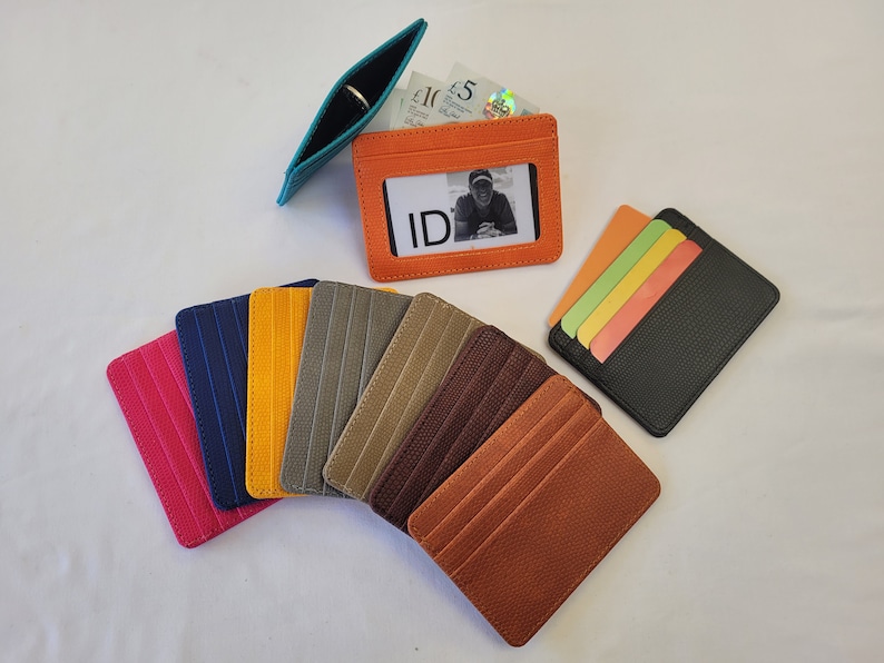 May include: Assortment of leather card holders in various colors, including orange, brown, gray, blue, and pink. Some card holders have a clear window for an ID card.  The text "ID" is visible on one of the card holders.