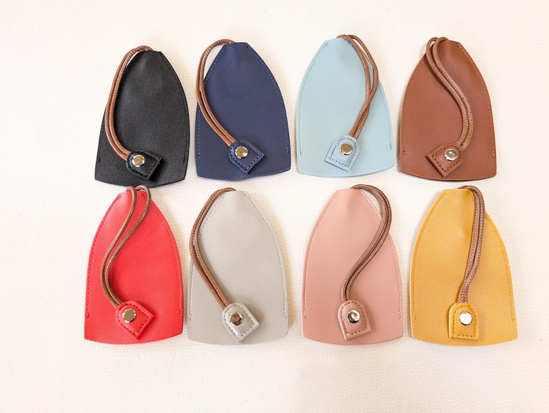 May include: Eight leather keychains in various colors, including black, navy blue, light blue, brown, red, gray, pink, and yellow. Each keychain has a loop and a button closure.