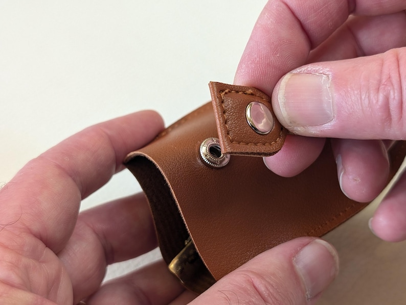 May include: A brown leather wallet with a flap closure and two silver snaps. The flap is folded back to reveal the interior of the wallet.