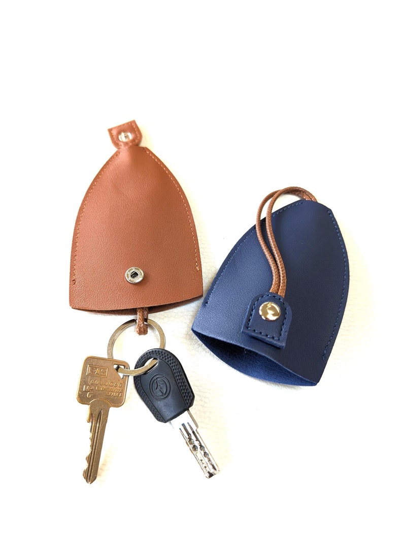 May include: Two keychains, one brown and one blue, with a key ring and two keys attached. The keychains are made of leather and have a snap closure.