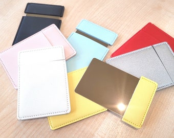 May include: A set of small, rectangular mirrors with different colored leather covers. The covers are in shades of pink, white, blue, red, gray, and yellow. The mirrors are all the same size and shape.