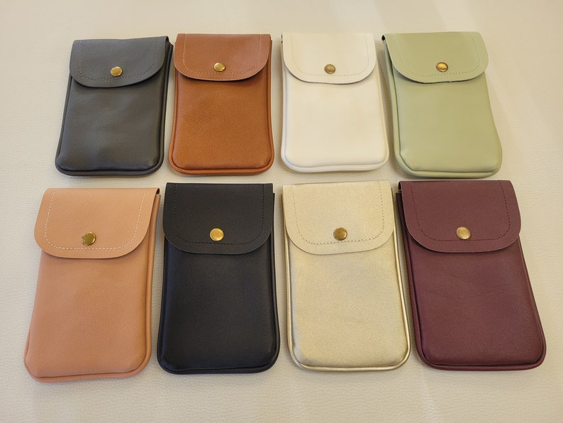 May include: Eight different colored phone cases with a small flap and a gold button. The cases are made of a soft, textured material.