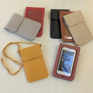 May include: Assortment of phone cases in various colors, including gray, brown, yellow, and red. Some cases have a clear plastic window for viewing the phone screen. One case has a strap for carrying over the shoulder.