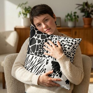 May include: A decorative pillow with a patchwork design featuring black and white animal prints. The pillow includes giraffe spots, zebra stripes, and leopard spots. The pillow is square and has a white background.