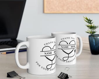 May include: Two white ceramic mugs with black handles. Both mugs feature a black and white graphic of a stethoscope in the shape of a heart with the text "Thank You" and "Name Here" on each mug.