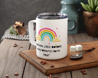 May include: White ceramic travel mug with a rainbow and the text "Bringing Lives: Donors Make Dreams Come True!"