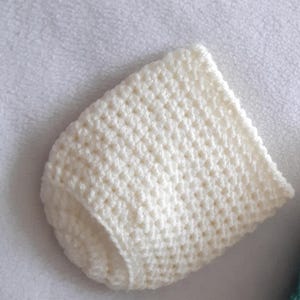 May include: Cream-coloured, crocheted baby hat. The hat is handmade with a textured stitch, and has a rounded crown and a folded brim. The hat is made of soft yarn, and is likely for a newborn or infant.