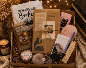 May include: A gift box containing a canvas pouch with the text MY WEEKEND IS ALL BOOKED, a glass tumbler with the text BOOKS ARE MY THERAPY, a brown paper-wrapped mystery book, a candle, a small pink pouch, a notepad, a pen, and a butterfly clip.