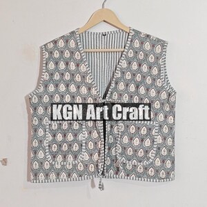 May include: A gray and white patterned sleeveless vest with a tie closure. The vest has a striped lining and two pockets. The text "KGN Art Craft" is printed on the front of the vest.