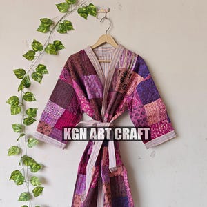 May include: A pink and purple patchwork robe with a white sash. The robe is made of quilted fabric and has a traditional Japanese kimono style. The text "KGN ART CRAFT" is visible on the robe.