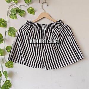 May include: Black and white striped shorts with an elastic waistband. The shorts are hanging on a wooden hanger. The text "KGN ART CRAFT" is visible on the shorts.