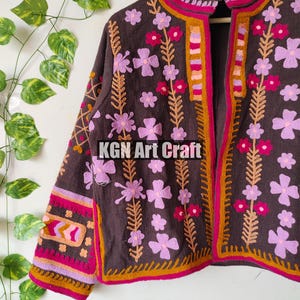 Puede incluir: Una chaqueta marr&oacute;n bordada con cuello alto y dise&ntilde;o floral. La chaqueta tiene un patr&oacute;n floral rosa, naranja y amarillo sobre un fondo marr&oacute;n. La chaqueta se cierra con una cremallera.