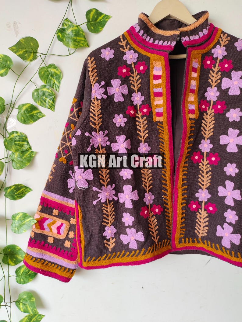 Puede incluir: Una chaqueta marr&oacute;n bordada con cuello alto y dise&ntilde;o floral. La chaqueta tiene un patr&oacute;n floral rosa, naranja y amarillo sobre un fondo marr&oacute;n. La chaqueta se cierra con una cremallera.
