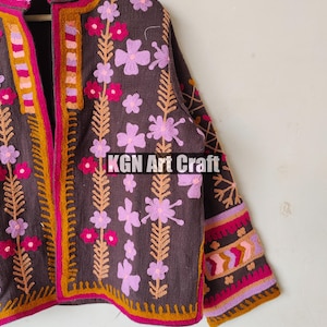 Puede incluir: Una chaqueta marr&oacute;n bordada con dise&ntilde;os florales de color rosa, morado y naranja. La chaqueta tiene un cuello alto y una cremallera frontal. El texto "KGN Art Craft" es visible en la chaqueta.