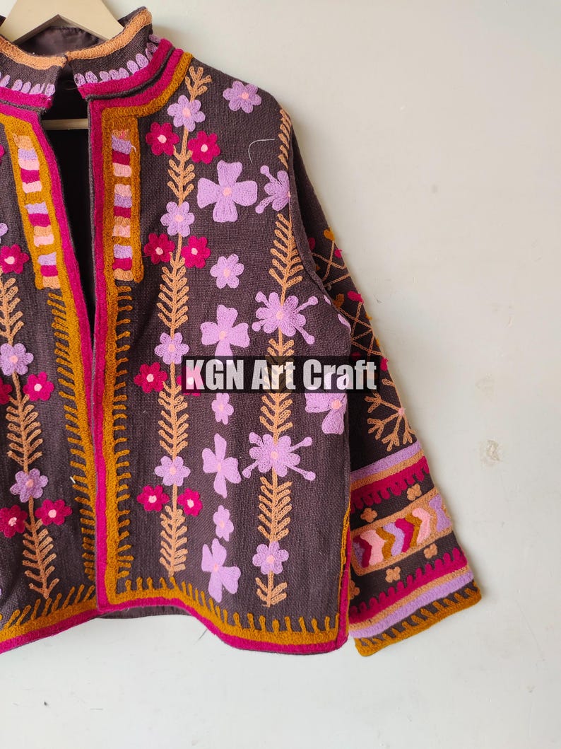 Puede incluir: Una chaqueta marr&oacute;n bordada con dise&ntilde;os florales de color rosa, morado y naranja. La chaqueta tiene un cuello alto y una cremallera frontal. El texto "KGN Art Craft" es visible en la chaqueta.