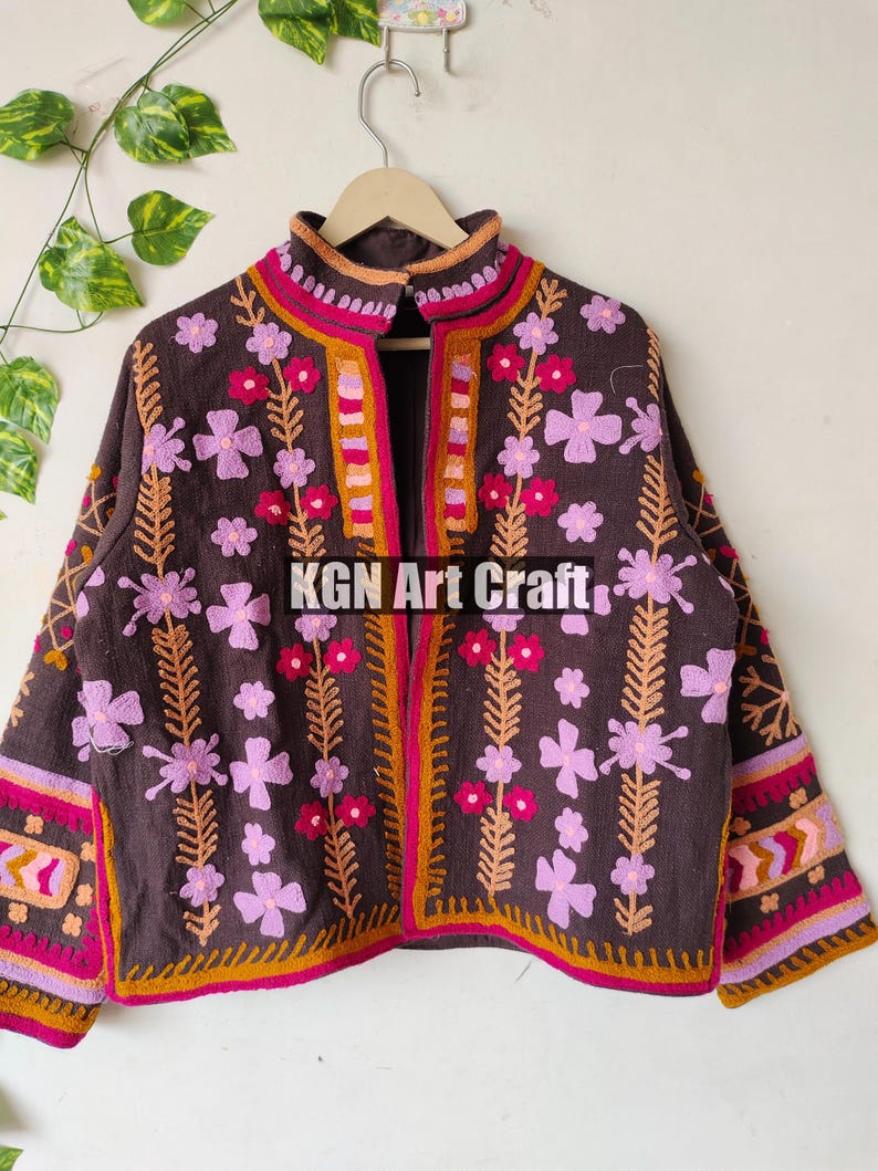 Puede incluir: Una chaqueta marr&oacute;n bordada con dise&ntilde;os florales rosas y naranjas. La chaqueta tiene un cuello alto y una cremallera. El texto "KGN Art Craft" est&aacute; bordado en la parte delantera de la chaqueta.