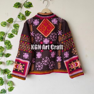 Puede incluir: Una chaqueta marr&oacute;n bordada con motivos florales rosas, rojos y naranjas. La chaqueta tiene cuello alto y mangas largas. El texto "KGN Art Craft" est&aacute; bordado en la parte posterior de la chaqueta.