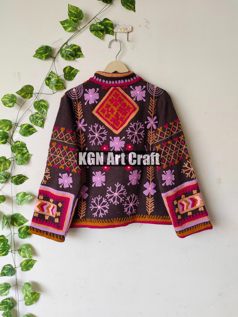 Puede incluir: Una chaqueta marr&oacute;n bordada con motivos florales rosas, rojos y naranjas. La chaqueta tiene cuello alto y mangas largas. El texto "KGN Art Craft" est&aacute; bordado en la parte posterior de la chaqueta.