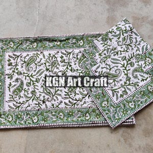 Può includere: Set di quattro tovaglioli di cotone verde e bianco con un motivo paisley. I tovaglioli hanno un bordo verde e sono piegati in una pila.