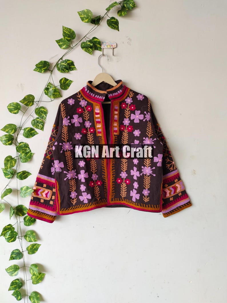 Puede incluir: Una chaqueta marr&oacute;n bordada con dise&ntilde;os florales de color rosa y rojo. La chaqueta tiene un cuello alto y mangas largas. El texto "KGN Art Craft" es visible en la parte delantera de la chaqueta.