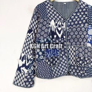May include: A blue and white patchwork quilted jacket with a V-neck and long sleeves. The jacket has a unique design with different patterns and textures.