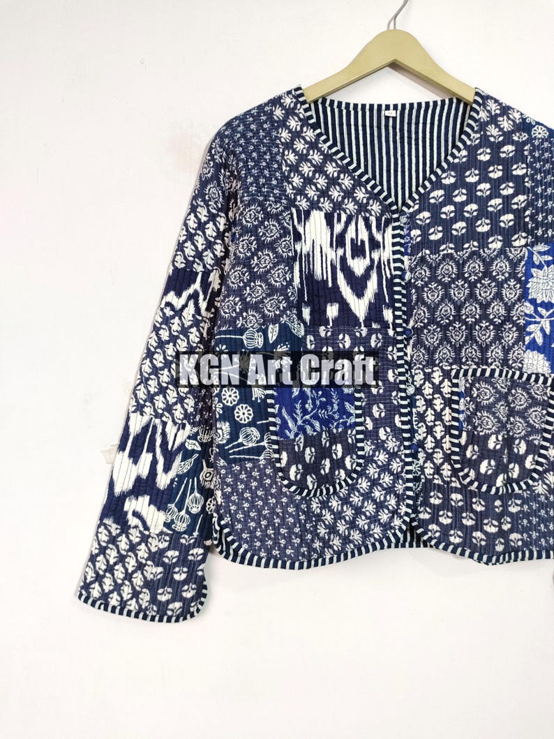 May include: A blue and white patchwork quilted jacket with a V-neck and long sleeves. The jacket has a unique design with different patterns and textures.