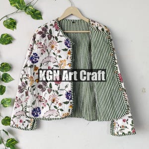 Może przedstawiać: Rewersyjna pikowana kurtka z kwiatowym nadrukiem po jednej stronie i zielono-białymi paskami po drugiej. Kurtka ma okrągły dekolt i długie rękawy. Tekst "KGN Art Craft" jest nadrukowany na przodzie kurtki.
