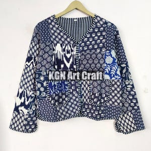 May include: A blue and white patchwork jacket with a V-neck and long sleeves. The jacket is made of cotton and has a quilted design. The jacket has a pocket on the left side and the text "KGN Art Craft" is printed on the front.