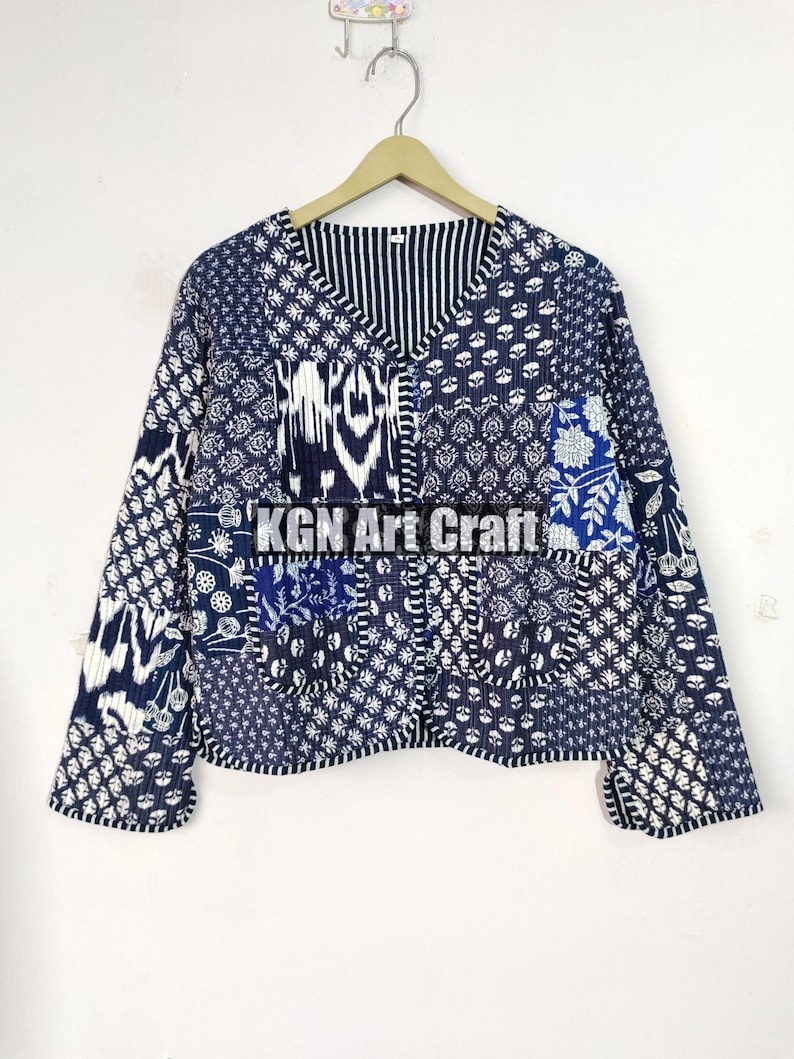 May include: A blue and white patchwork jacket with a V-neck and long sleeves. The jacket is made of cotton and has a quilted design. The jacket has a pocket on the left side and the text "KGN Art Craft" is printed on the front.