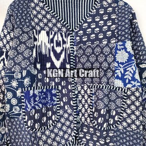 May include: A blue and white patchwork jacket with a button closure and a pocket on the front. The jacket is made of cotton and has a quilted design. "KGN Art Craft" is printed on the jacket.