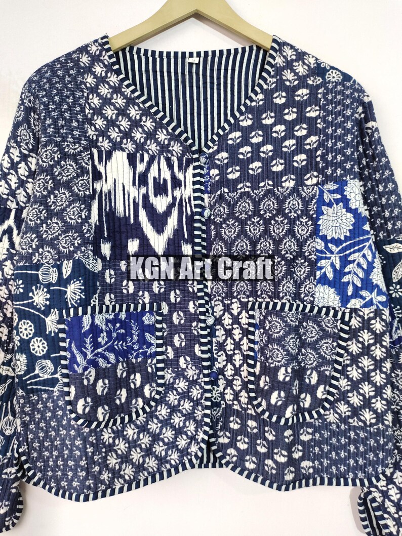 May include: A blue and white patchwork jacket with a button closure and a pocket on the front. The jacket is made of cotton and has a quilted design. "KGN Art Craft" is printed on the jacket.