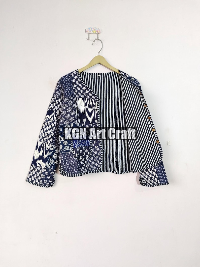 May include: A blue and white patterned cotton jacket with a striped lining. The jacket has a V-neck and long sleeves. The jacket is hanging on a wooden hanger.