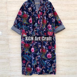 May include: A long, navy blue robe with a floral print. The robe has a contrasting black and white striped lining on the sleeves and collar. The robe is hanging on a hanger.