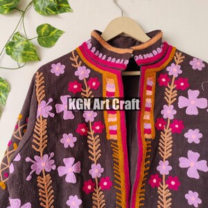Puede incluir: Una chaqueta marr&oacute;n bordada con dise&ntilde;os florales de color rosa, naranja y rojo. La chaqueta tiene un cuello alto y una cremallera frontal. El texto "KGN Art Craft" es visible en la parte delantera de la chaqueta.