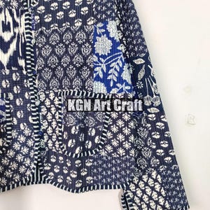 May include: A blue and white patchwork jacket with a button closure and long sleeves. The jacket is made of cotton and has a quilted design. The fabric features a variety of floral and geometric patterns. The text "KGN Art Craft" is visible on the jacket.