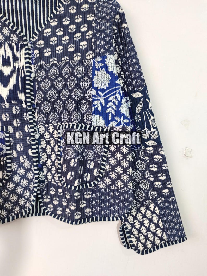 May include: A blue and white patchwork jacket with a button closure and long sleeves. The jacket is made of cotton and has a quilted design. The fabric features a variety of floral and geometric patterns. The text "KGN Art Craft" is visible on the jacket.
