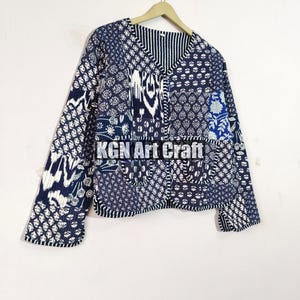 May include: A blue and white patchwork quilted jacket with a V-neck and long sleeves. The jacket has a variety of floral and geometric patterns.