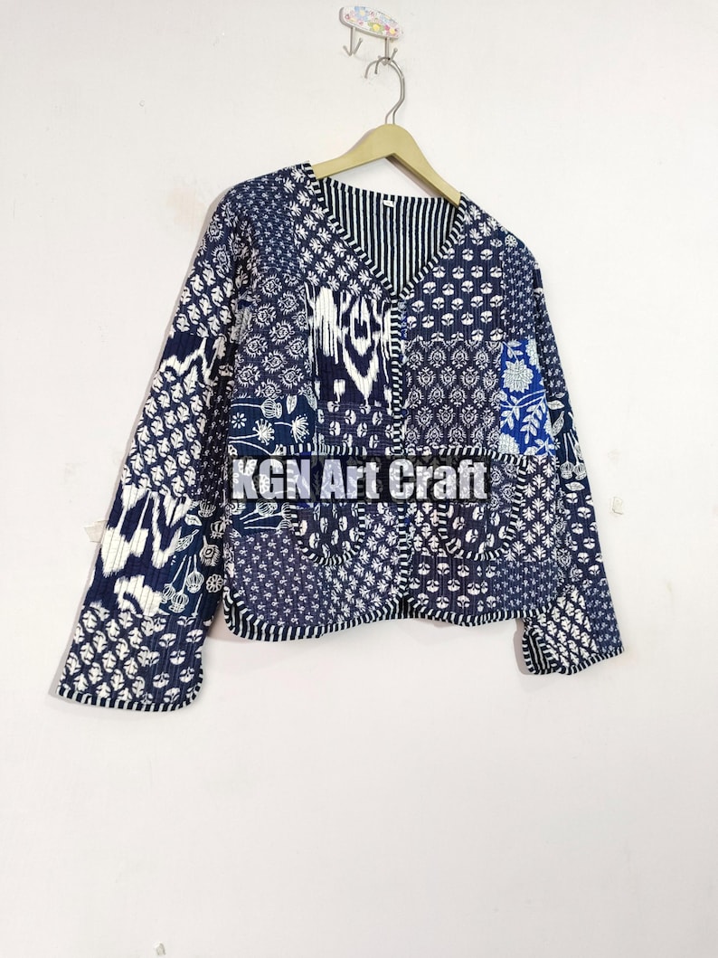 May include: A blue and white patchwork quilted jacket with a V-neck and long sleeves. The jacket has a variety of floral and geometric patterns.