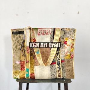 May include: A patchwork tote bag with yellow, brown, and white fabric. The bag has a long strap and is sitting on a metal stool. The text "KGN Art Craft" is visible on the bag.