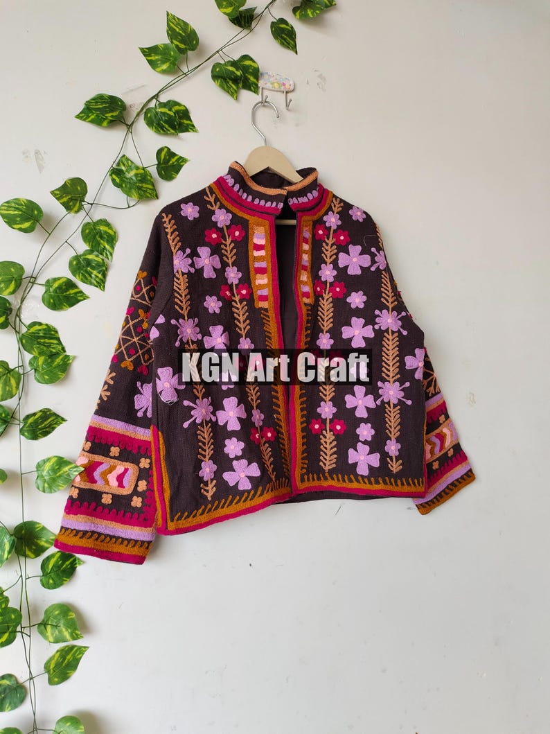 Puede incluir: Una chaqueta marr&oacute;n bordada con dise&ntilde;os florales de color rosa, naranja y blanco. La chaqueta tiene un cuello alto y cierre de bot&oacute;n. El texto "KGN Art Craft" es visible en la parte delantera de la chaqueta.