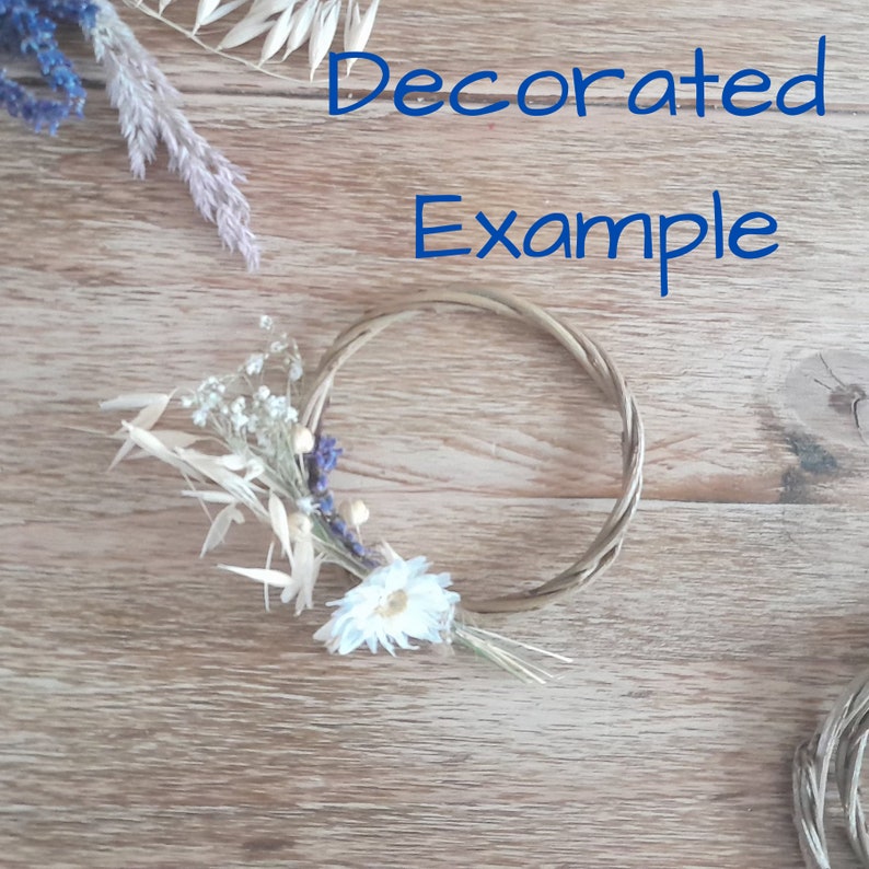 May include: A natural woven wreath decorated with dried flowers, including white daisies, lavender, and oat stalks. The wreath is on a wooden surface.