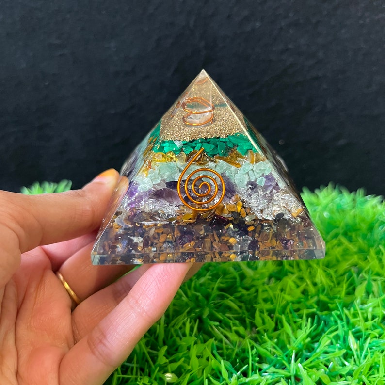 May include: A clear pyramid made of layered crystals, including amethyst, tiger's eye, aventurine, clear quartz, and green aventurine. A copper wire coil is embedded in the centre of the pyramid.