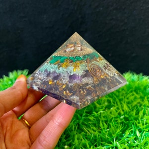 May include: A clear crystal pyramid with layers of different coloured crystals, including amethyst, green aventurine, tiger's eye, and malachite. A copper wire coil is embedded in the pyramid.