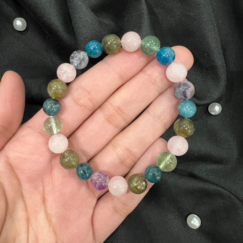 Op de afbeelding: Een veelkleurige edelsteen armband met roze, groene, blauwe en paarse kralen. De armband is gemaakt van natuurlijke stenen en is geregen op een doorzichtig elastisch koord.