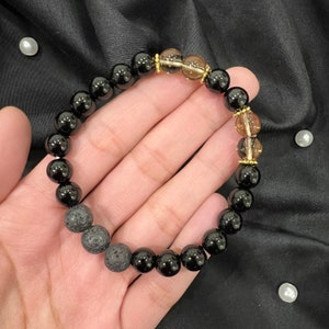 May include: Black and brown beaded bracelet with gold accents. The bracelet is made of black lava rock, black onyx, and brown tiger's eye beads.