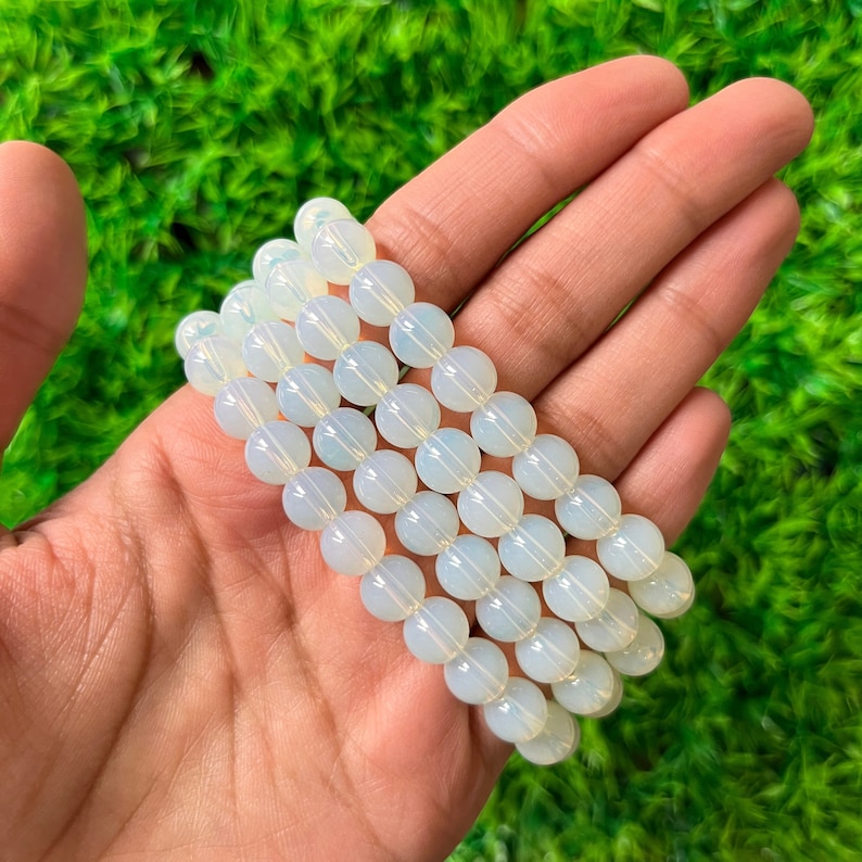 K&ouml;nnte beinhalten: Ein Stapel wei&szlig;er Opalperlenarmb&auml;nder. Die Perlen sind rund und glatt und haben einen leichten irisierenden Schimmer.